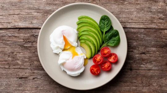Vue aérienne d'un petit-déjeuner équilibré avec œufs, avocat et légumes verts sur une table en bois naturel